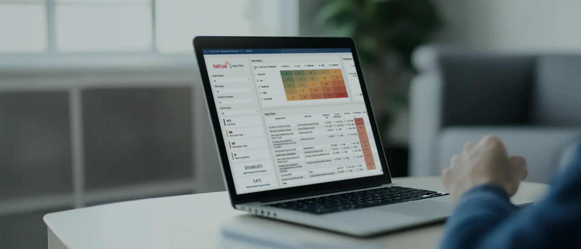A person uses a laptop displaying data analytics with colorful charts, graphs, and tables on the screen, set on a white desk in a bright, modern room.