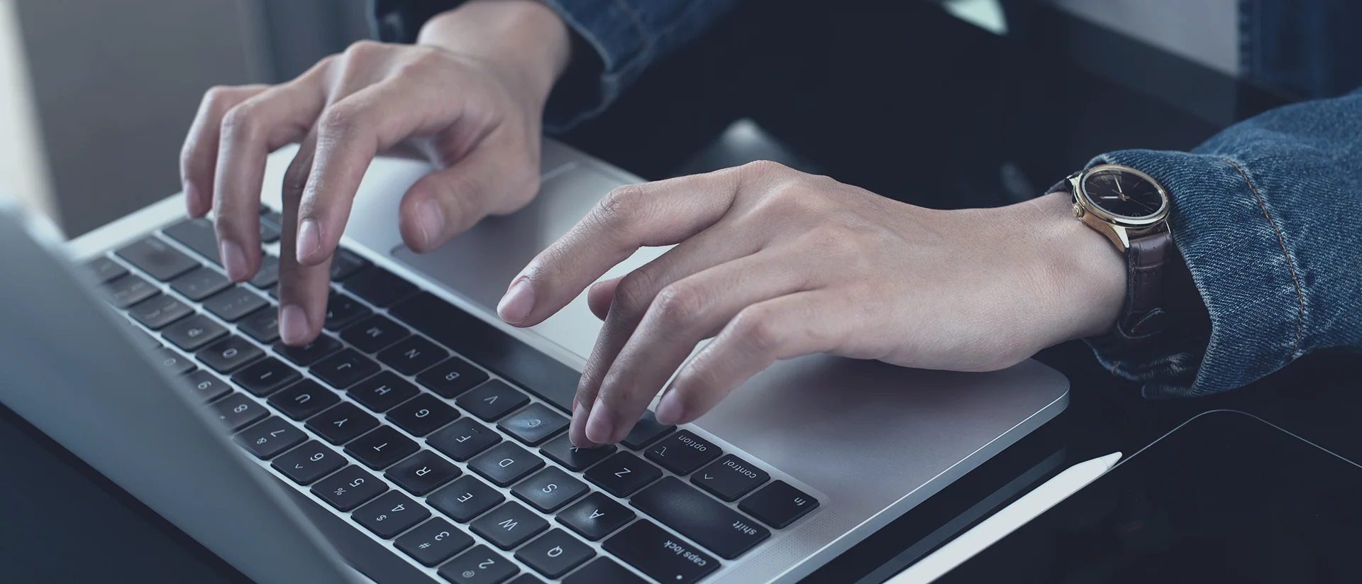 Close-up of a person’s hands typing on a laptop keyboard, with a wristwatch visible on one wrist.