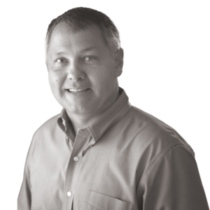Smiling man with short hair wearing a button-up shirt, facing the camera in a black and white portrait on a plain background.