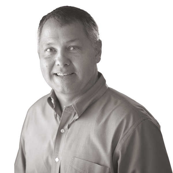 Smiling man with short hair wearing a button-up shirt, facing the camera in a black and white portrait on a plain background.