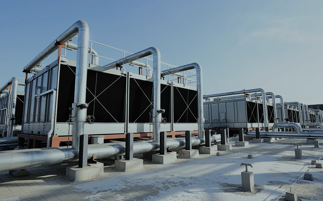 Rows of large industrial cooling units with metal pipes and support structures outdoors on a concrete surface under a clear blue sky.