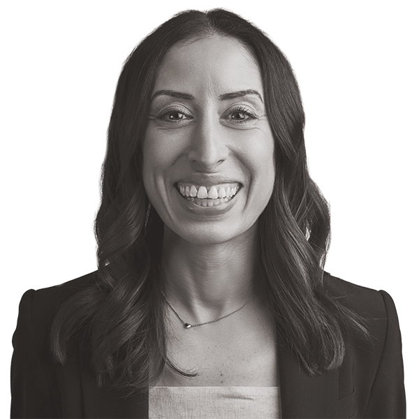 Smiling woman with long dark hair, wearing a blazer over a light top, facing the camera against a plain white background.