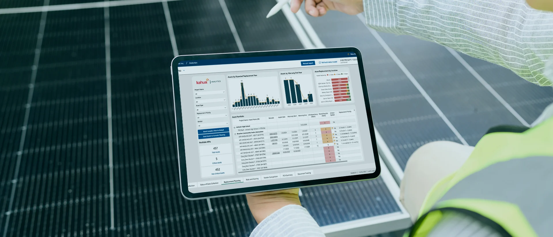 A person in a safety vest holds a tablet displaying data charts and graphs, with solar panels visible in the background.