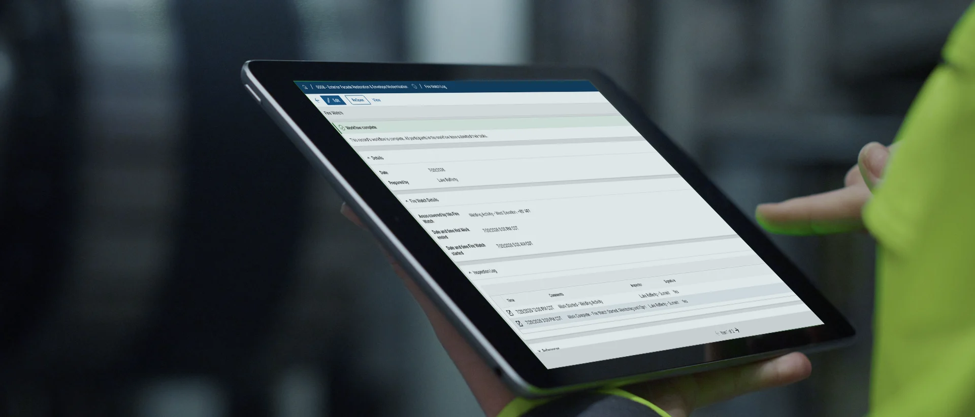 A person holding a tablet displaying a technical data sheet or form with several fields and tables visible on the screen.