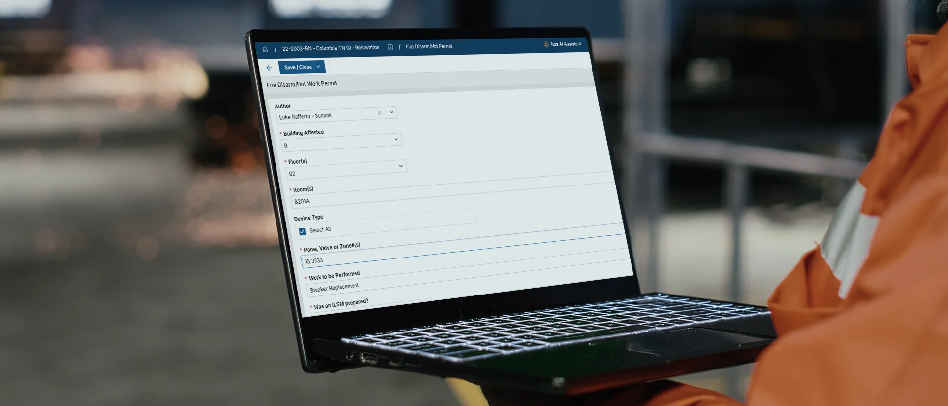 A person in an orange jacket holds a laptop showing a form titled Risk Factors New Hazard with various input fields and dropdown menus on the screen.