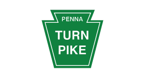 Green Pennsylvania Turnpike sign shaped like a keystone, with white text reading PENNA TURN PIKE on a light gray background.