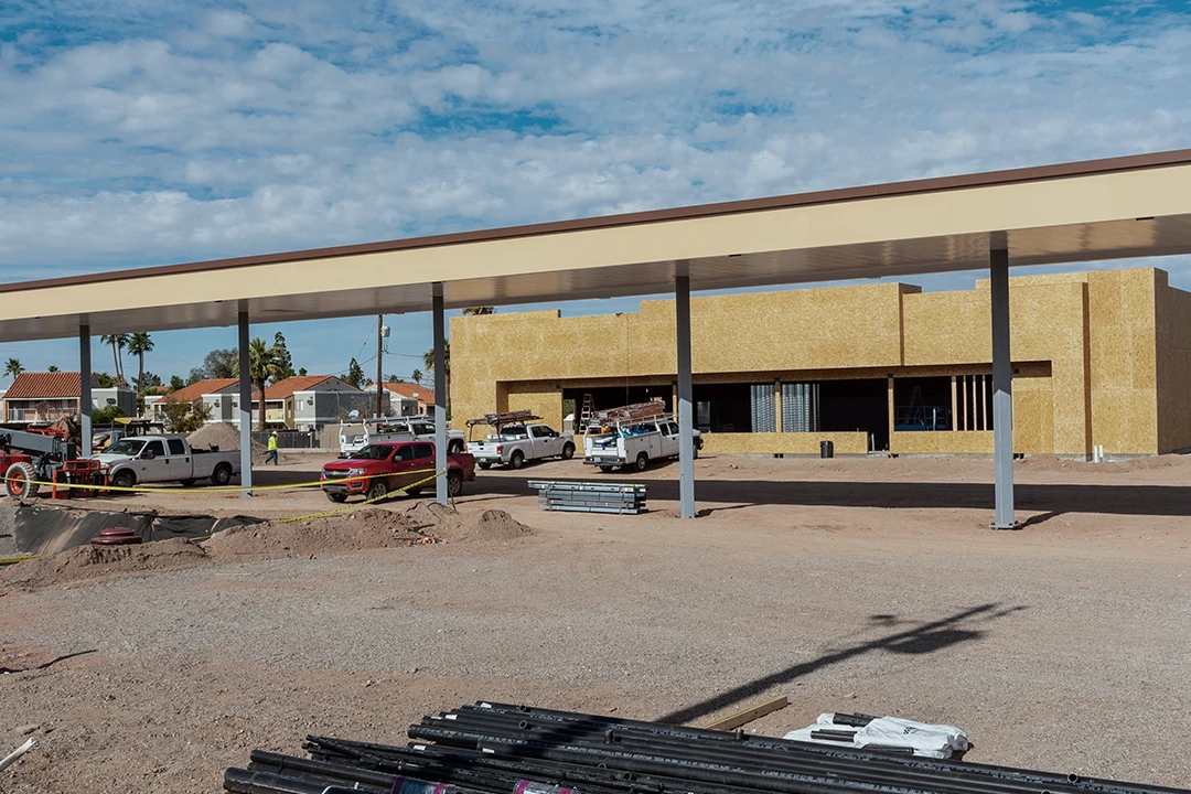 A construction site with a partially built commercial building, several work trucks, and construction materials, under a partly cloudy sky.