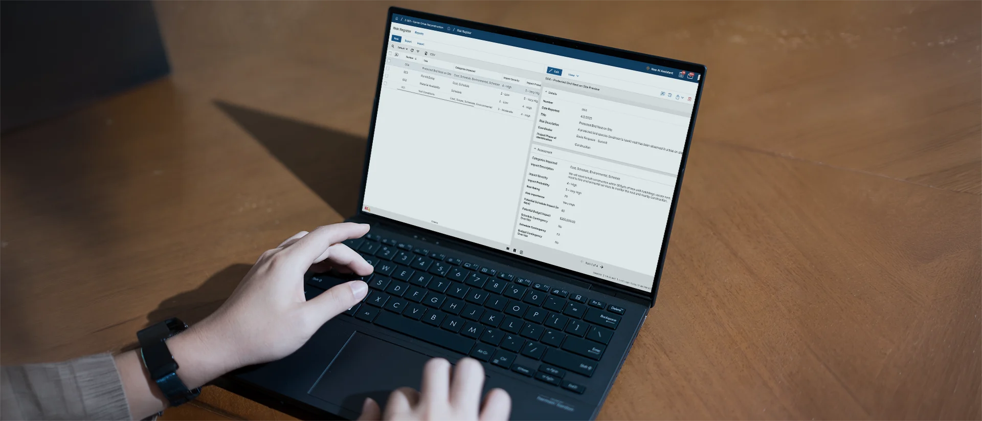 A person types on a black laptop displaying a data management or CRM software interface, seated at a wooden table.