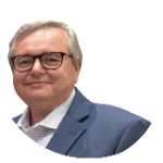 Smiling older man with glasses and gray hair, wearing a blue suit jacket and white shirt, standing against a plain white background.