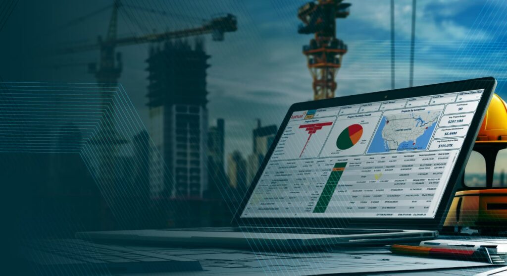 A laptop on a desk displays charts and maps on its screen, set against a construction site backdrop with cranes and buildings under construction. A yellow hard hat sits nearby.