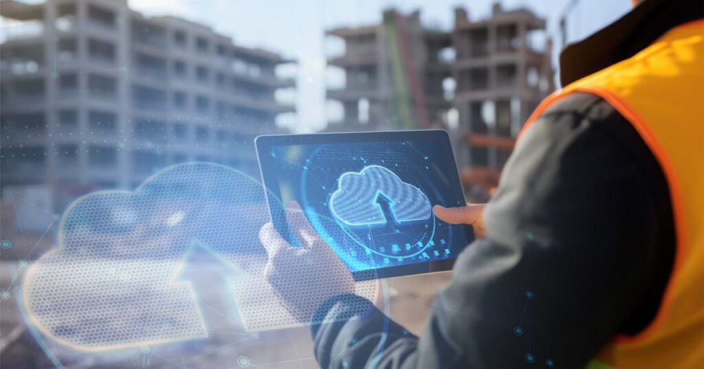 A construction worker uses a tablet with a digital cloud upload icon overlayed, while unfinished buildings are visible in the blurred background.