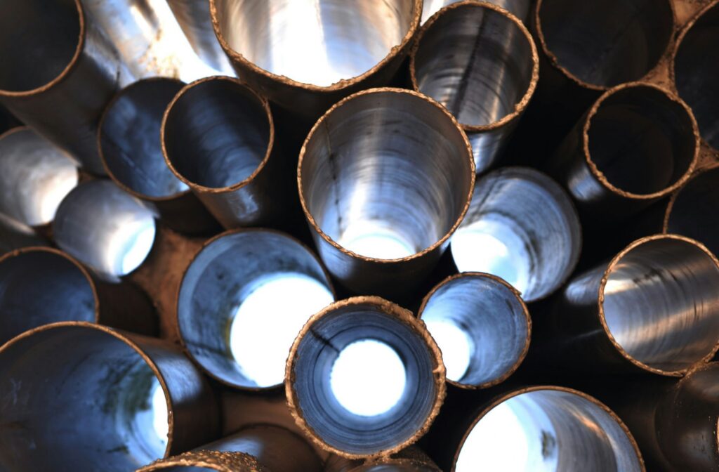 Close-up view looking into the ends of multiple metal pipes, arranged in a cluster, with bright light shining through from the other side, creating circular highlights.