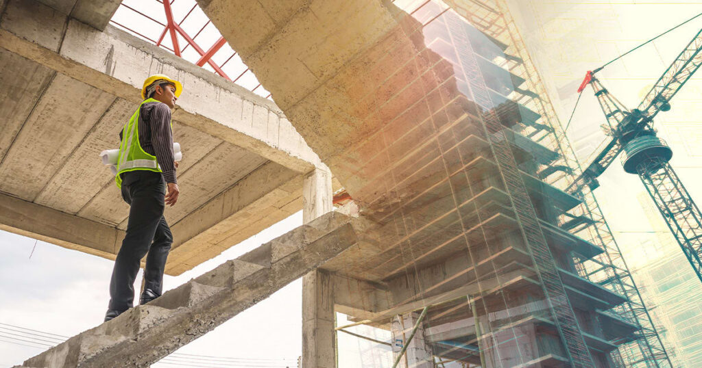 A construction worker wearing a hard hat and safety vest stands on concrete stairs, holding blueprints and looking at the unfinished building structure with a crane in the background.