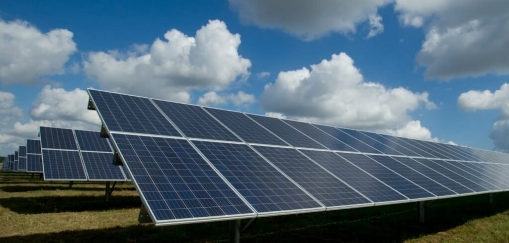Rows of solar panels in a field under a partly cloudy blue sky, capturing sunlight for renewable energy.