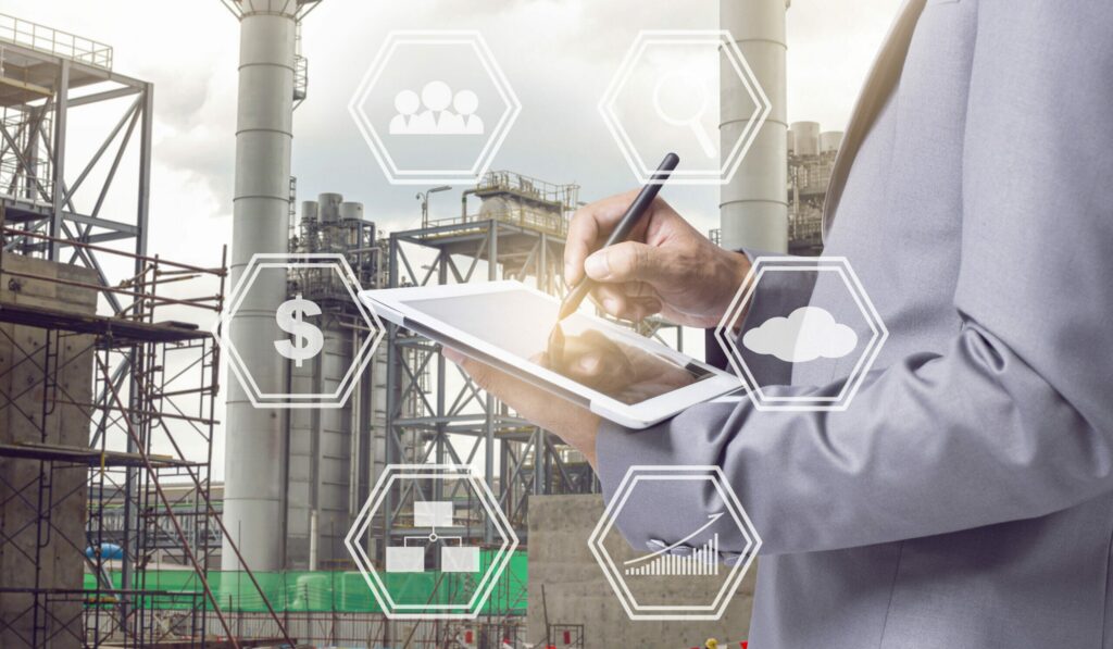 A person in a suit uses a stylus on a tablet, with industrial buildings in the background and transparent digital business icons overlaying the image.