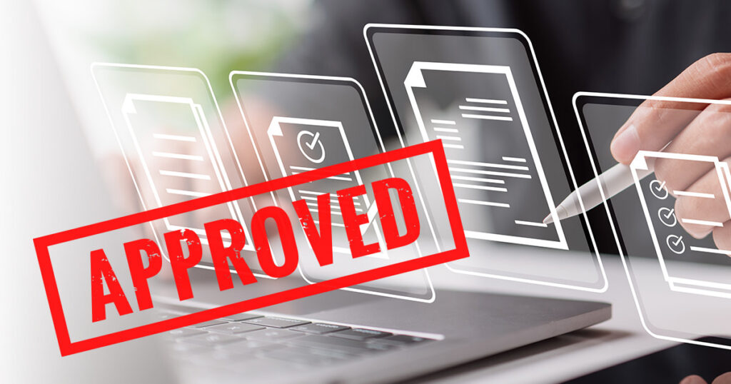 A hand holding a stylus points at digital documents on a laptop, with a large red APPROVED stamp overlaying the image, symbolizing approval of digital paperwork.