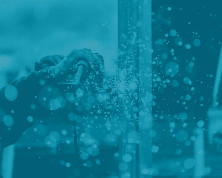 A close-up of a person using a power tool, creating sparks and debris, with a blue overlay covering the entire image.