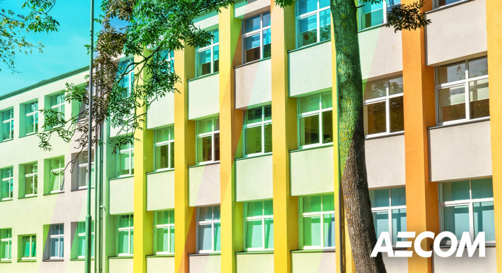 A modern, multi-story building with yellow and orange vertical accents, many windows, trees in front, and the AECOM logo in the lower right corner.