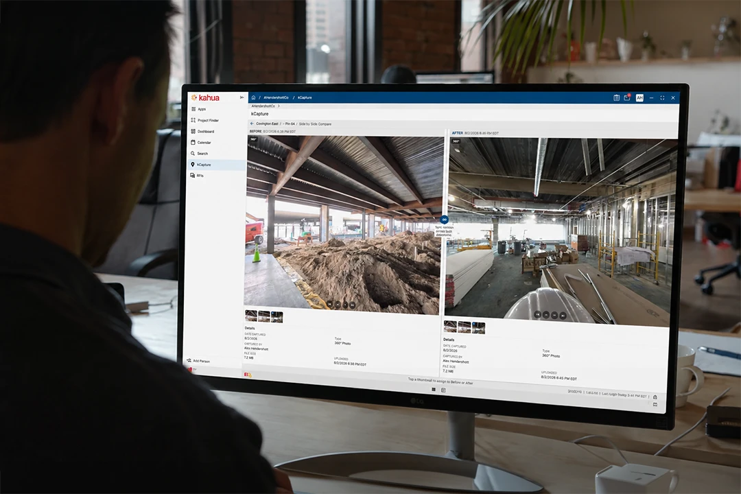 A person views construction site progress photos on a desktop monitor, showing two side-by-side images of an indoor building area under construction with exposed beams and equipment.
