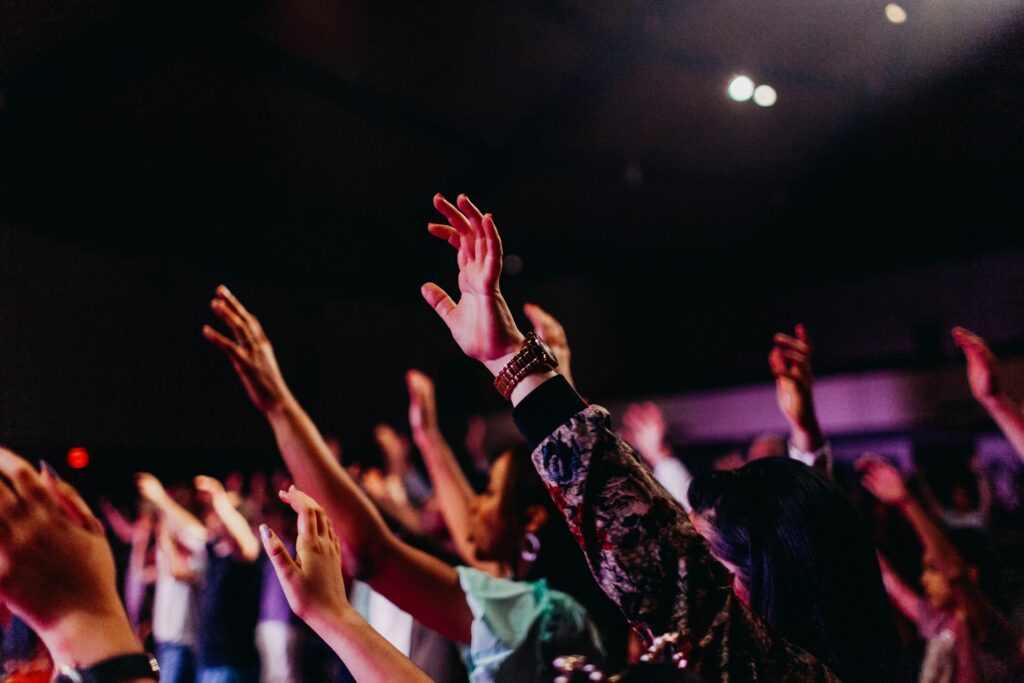 A crowd of people in a dark room with their hands raised in the air.