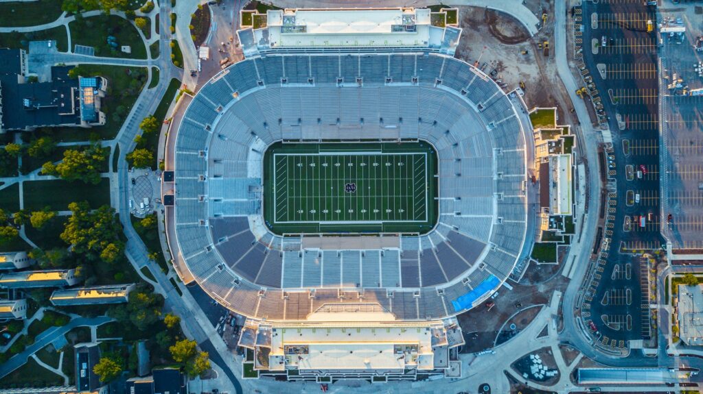 Aerial view of a large football stadium with a central field and surrounding bleachers, situated among campus buildings and parking lots.